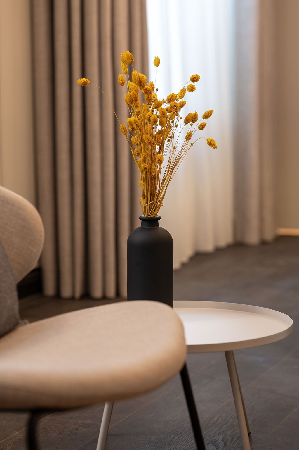 A modern room with a round table and a chair, a vase with yellow flowers, and a window with curtains.