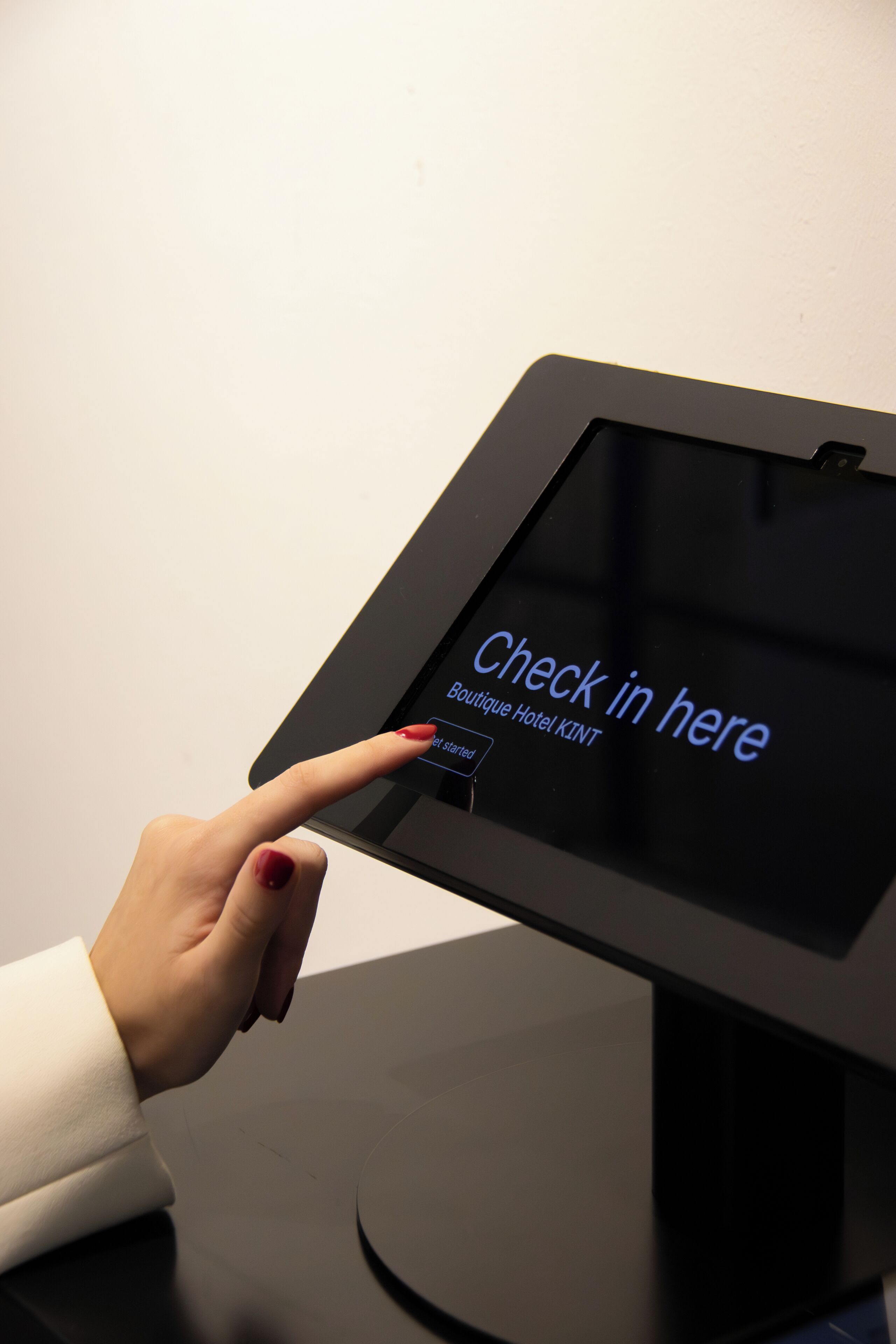 A digital kiosk with a screen displaying 'Check in here' and 'Boutique Hotel KINT' text.