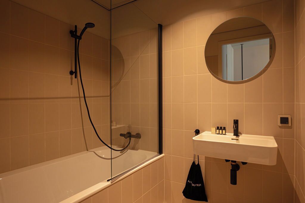 A bathroom with a glass-enclosed shower, a white sink, and a round mirror.