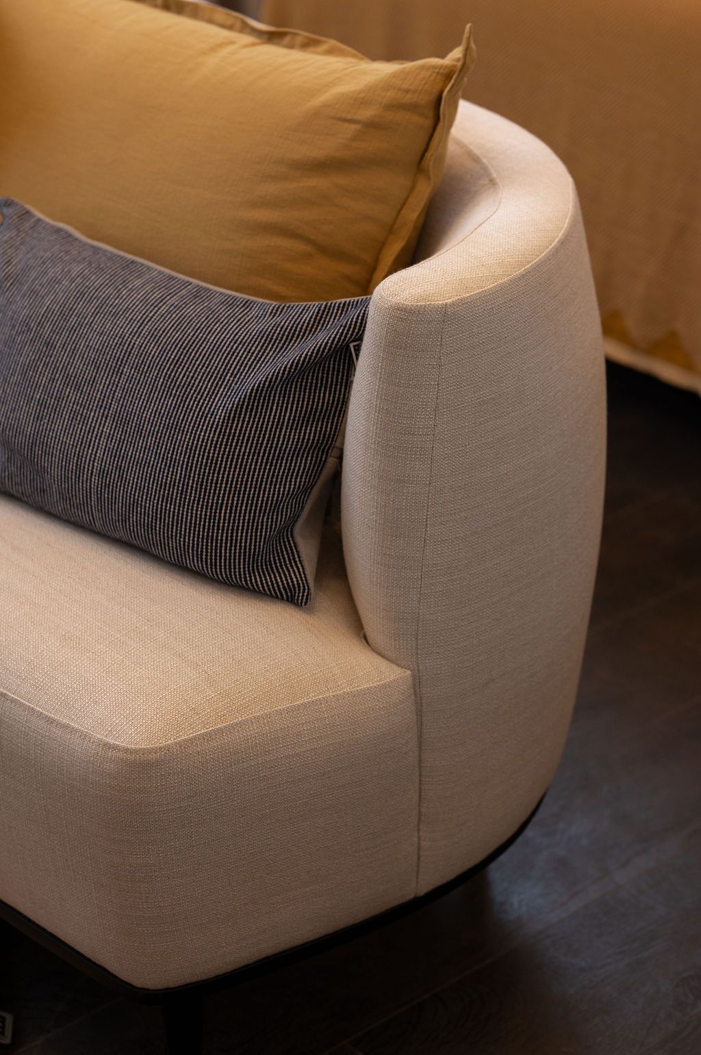 A corner of a sofa with a light-colored fabric and a dark striped pillow.