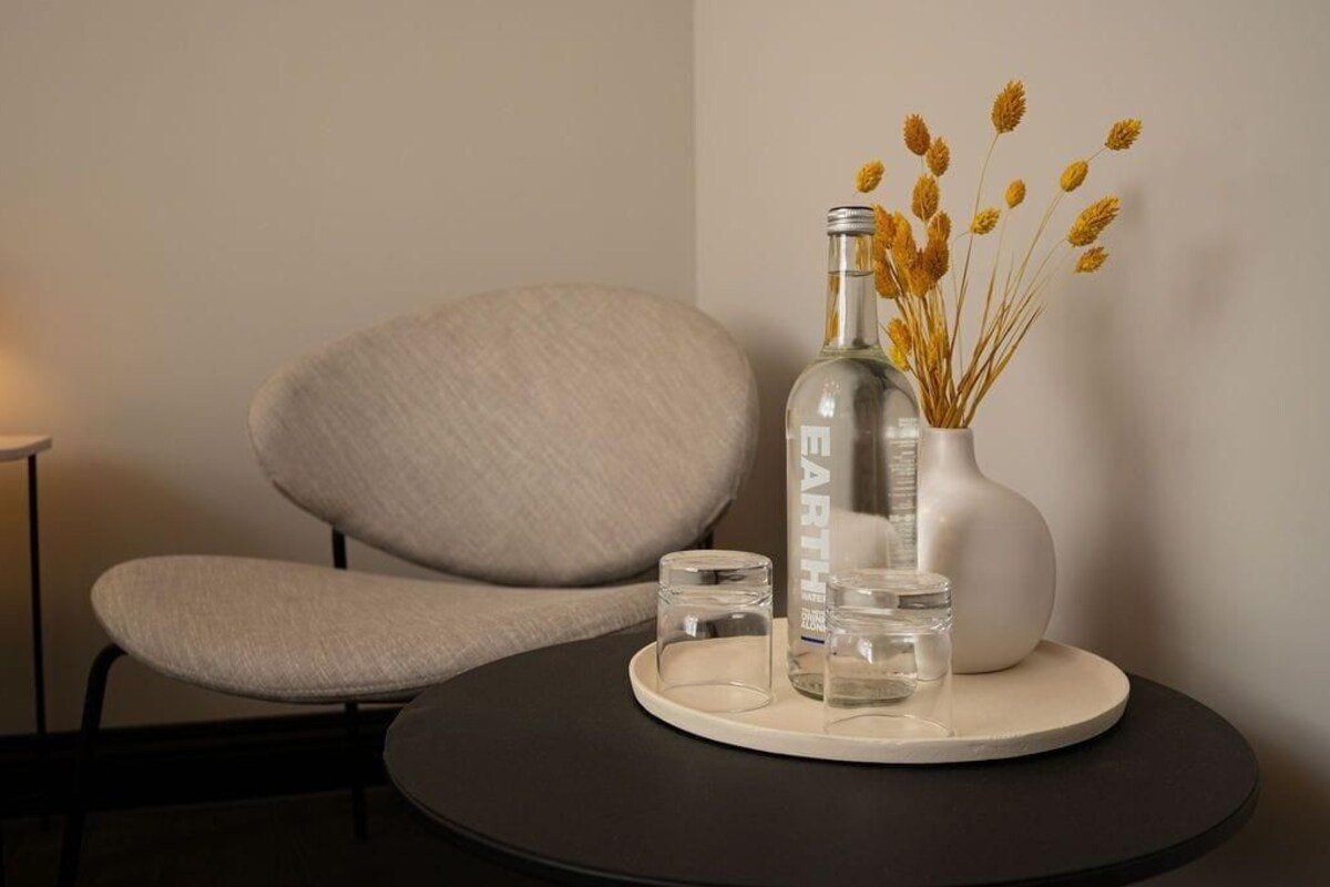 Una habitación moderna con una mesa redonda, una silla, una botella y un jarrón con flores secas.
