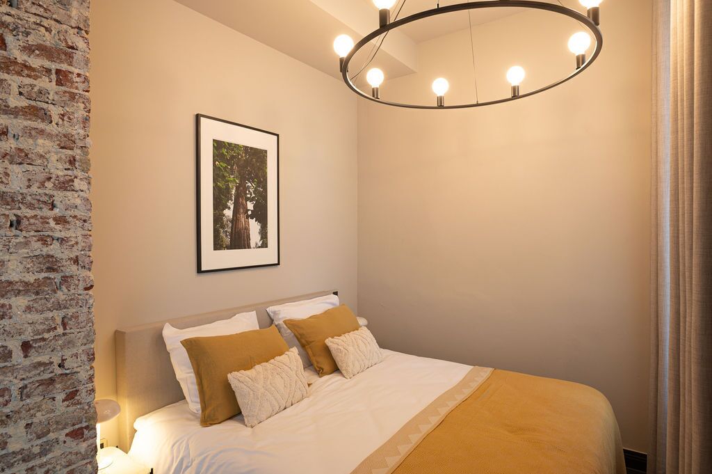 Ein Schlafzimmer mit einem Bett, einem gerahmten Bild an der Wand und einer runden Leuchte darüber.