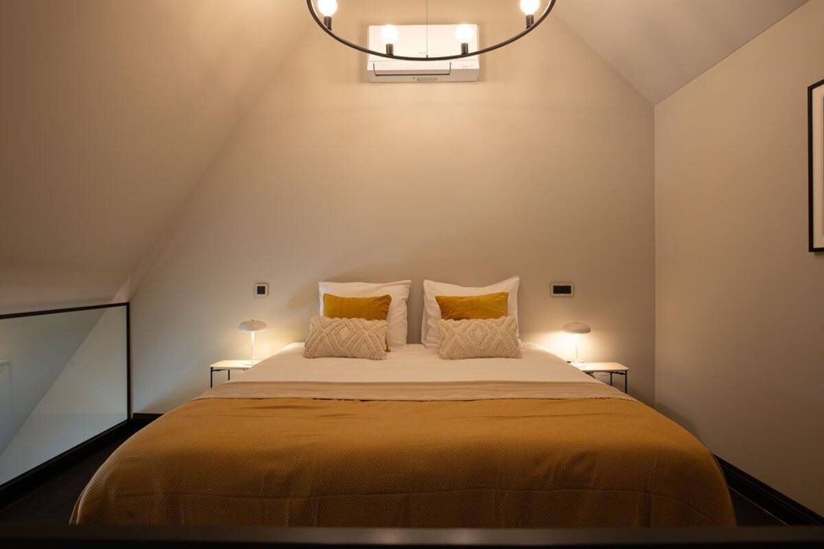 Quarto com uma cama, duas luminárias de apoio, iluminação no teto e uma janela.