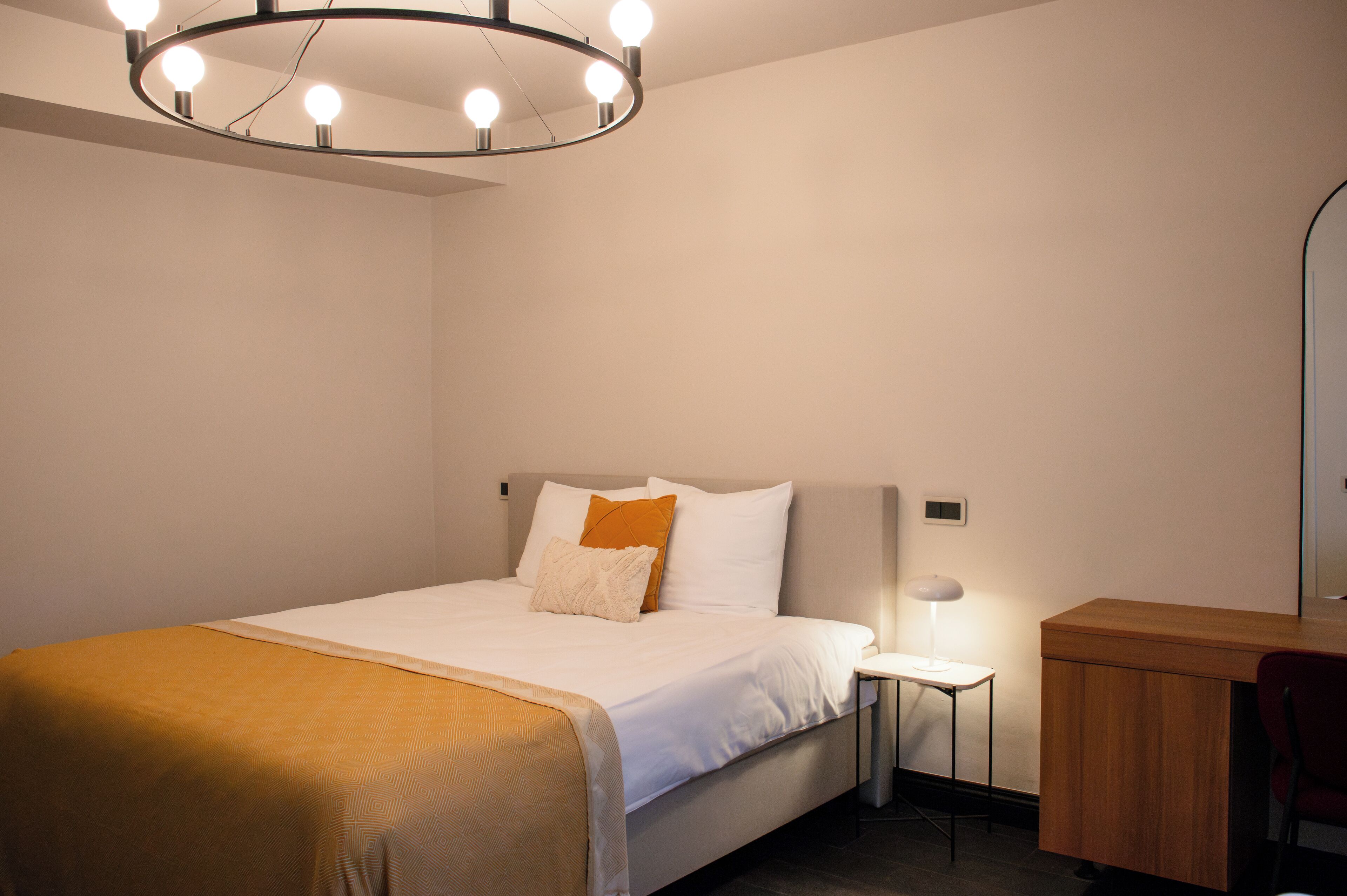 Un dormitorio moderno con cama, mesita de noche y espejo.