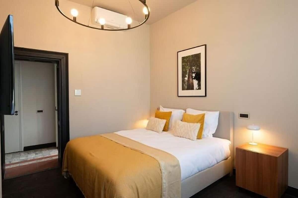 Quarto de hotel com cama, abajur e um quadro na parede.