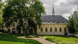 A historic building with a central tower, arched windows, and a courtyard with a pathway. - Hotel Kint (Valkenburg aan de Geul)