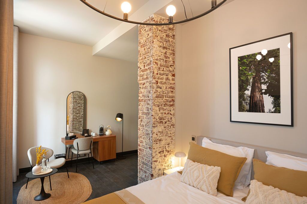 Habitación de hotel con cama, escritorio y una silla. Se aprecia una pared de ladrillo y un cuadro enmarcado.