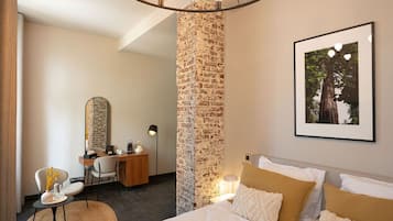 Habitación de hotel con cama, escritorio y una silla. Se aprecia una pared de ladrillo y un cuadro enmarcado.