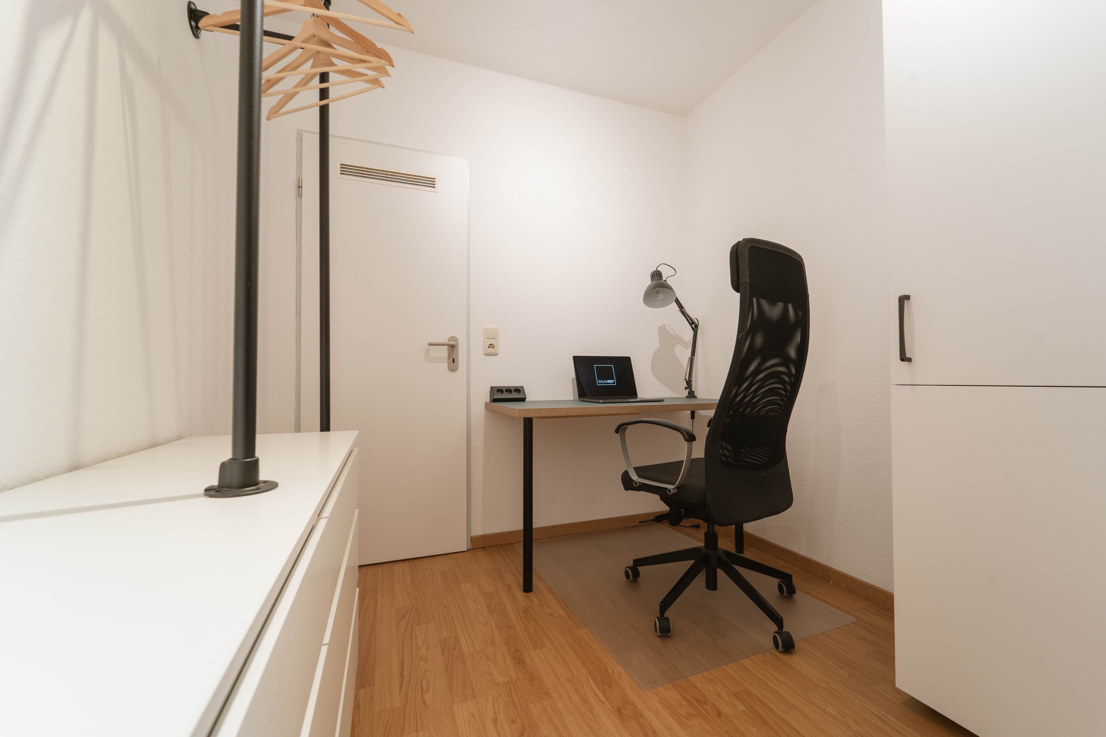 Une petite pièce propre, équipée d’un bureau, d’une chaise et d’une lampe.