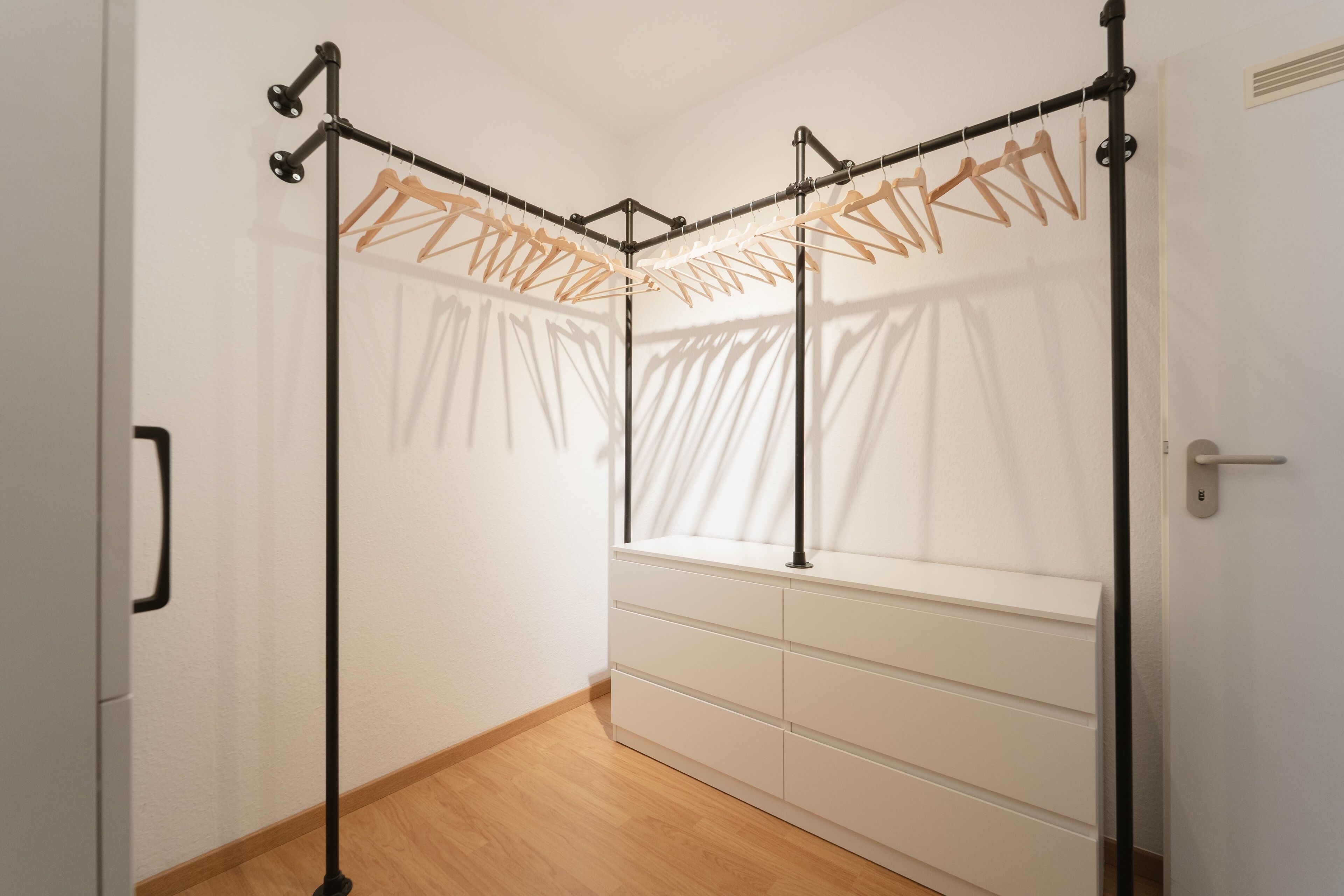 A room with a built-in wardrobe, a window with sheer curtains, and a wooden floor.