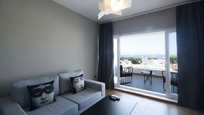 A modern living room with a grey sofa, two cushions, a black coffee table, and a large window with a view of the city. - Smart City Suites Bodrum (Bodrum)