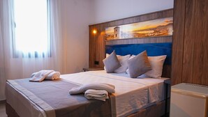 A neatly made bed with pillows and towels, a wooden headboard with a painting, and a small bedside table. - Smart City Suites Bodrum (Bodrum)