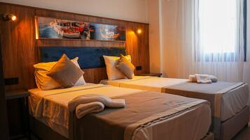 Habitación de hotel con dos camas, cabecero de madera, obra de arte que representa barcos y un ventanal con cortinas.