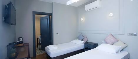 A modern hotel room with two single beds, a desk, a chair, a TV, and an air conditioning unit.