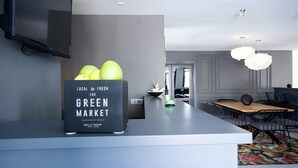 Eine moderne Küche mit grauer Arbeitsplatte, einer schwarzen Kiste mit der Aufschrift 'Local & Fresh The Green Market' und einem Essbereich mit Holztisch und Stühlen.
