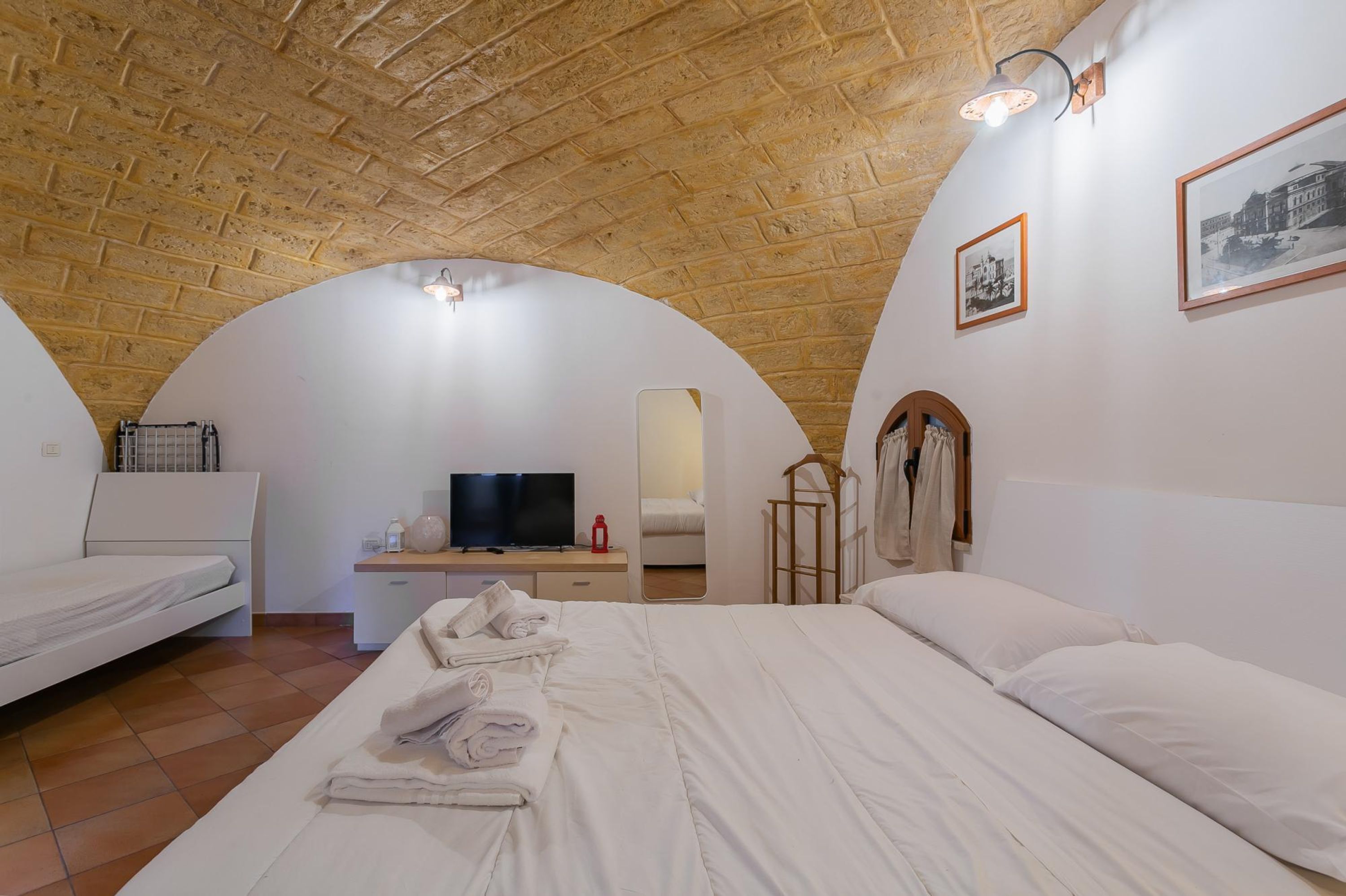 A bedroom with a brick ceiling, a bed, a TV, a desk, and a mirror.