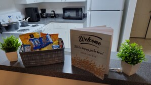 Una encimera de cocina con un cartel de bienvenida, una cesta de aperitivos y dos macetas con plantas.