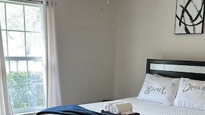 Un dormitorio con cama, ventilador de techo, ventana con cortinas y una obra de arte en la pared.