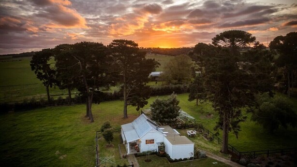 Une maison de campagne avec un grand jardin, entourée d’arbres et de champs.