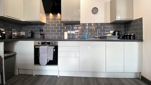 A modern kitchen with white cabinets, a black tiled backsplash, a built-in oven, and a microwave. - StayCrewe Apartments (Crewe)