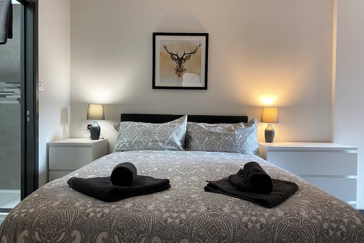 A neatly made bed with patterned bedding, two black towels, and a framed deer artwork on the wall.