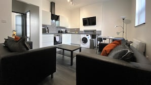 A modern living room with a sofa, a coffee table, and a TV mounted on the wall. - StayCrewe Apartments (Crewe)