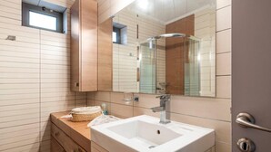 A modern bathroom with a large mirror, a white sink, wooden cabinets, and a small window. - Beautiful 1-bed Cottage in Megalopolis (Megalopolis)