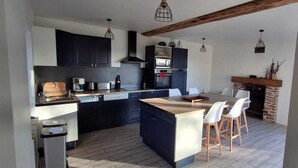 Une cuisine moderne avec des meubles sombres, un îlot central et une cheminée en pierre.