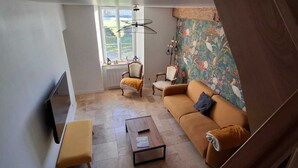 Un salon comprenant un canapé, un fauteuil et une table basse. Une fenêtre offre une vue sur la verdure à l’extérieur.