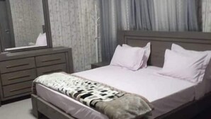 Een slaapkamer met een bed, een kast, een spiegel en gordijnen.
