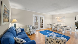 A living room with a blue sofa, patterned armchair, and a dining area with a white table and chairs. - Pet Friendly Private House w/Pool & Game Room + Free Attraction Tickets! (North Myrtle Beach)