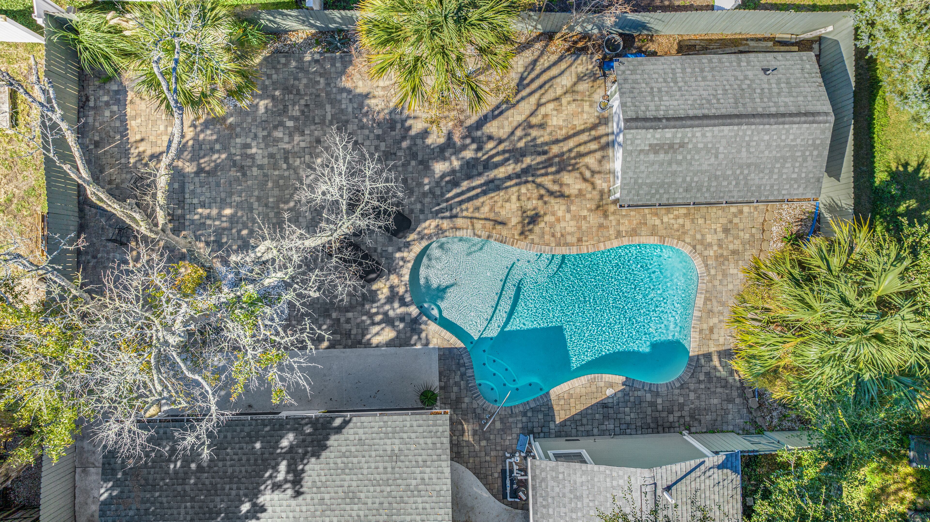 An aerial view of a residential area with a swimming pool, brick pathways, and surrounding vegetation.