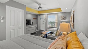Ein Schlafzimmer mit Bett, Schreibtisch, Stuhl, Deckenventilator und einem Fenster mit Jalousien.