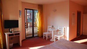 A hotel room with a bed, a desk with a television, a small table with chairs, and a sliding glass door to the balcony. - Guest House Anex (Bansko)