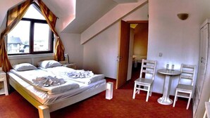 A bedroom with a bed, a window with curtains, a small table with chairs, and a door leading to another room. - Guest House Anex (Bansko)