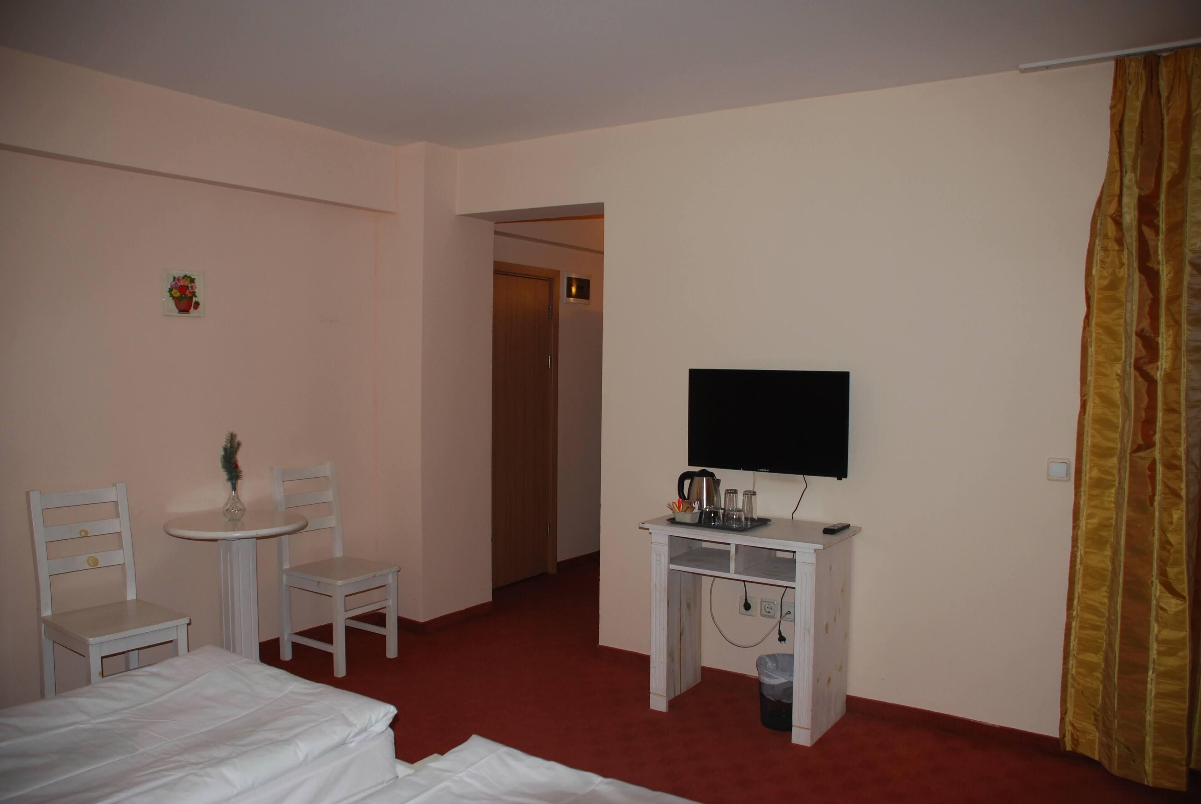 Ein Hotelzimmer mit Bett, Schreibtisch mit Fernseher, Stuhl, einem kleinen Tisch und einem Mülleimer.