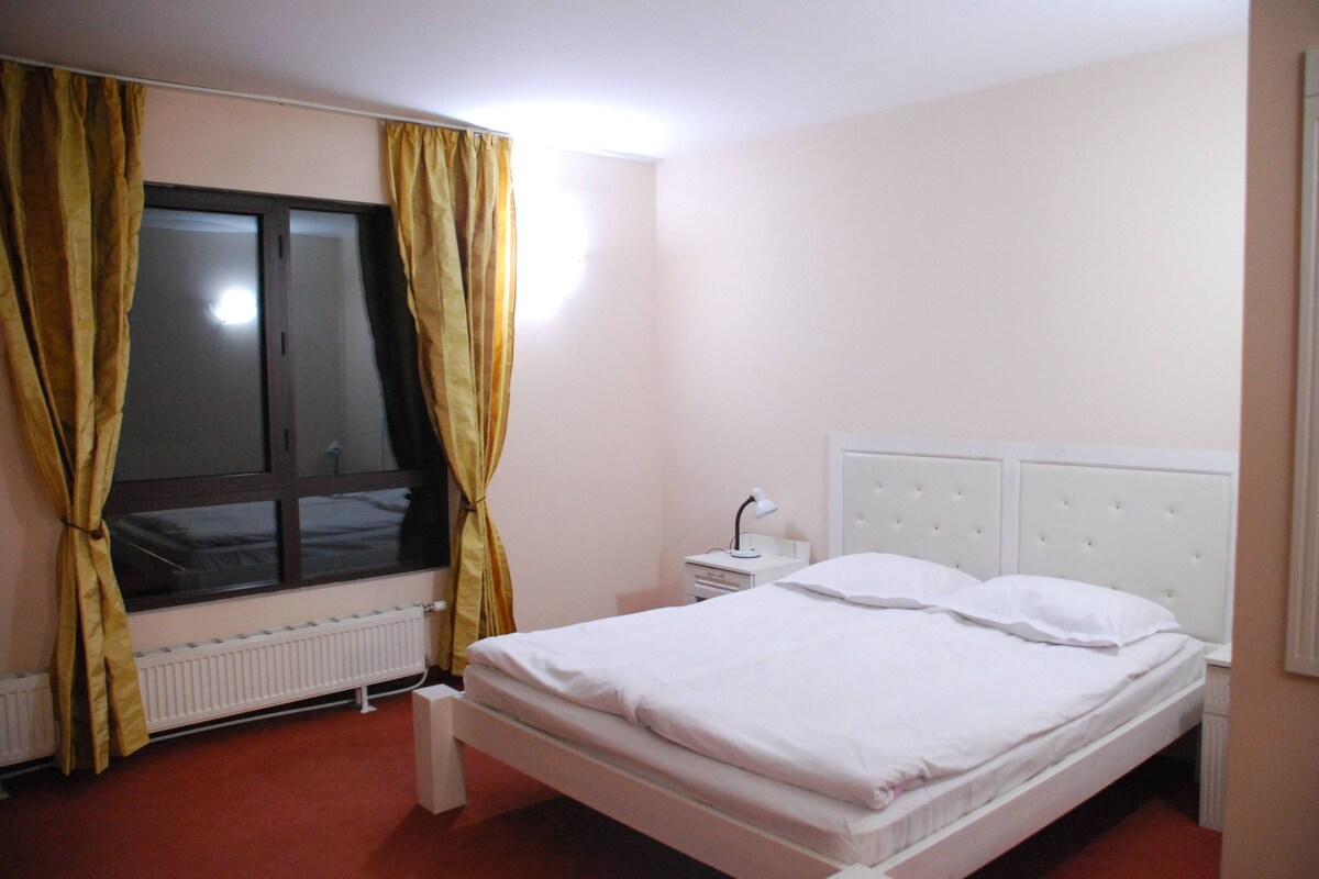 Un dormitorio con una cama individual, una mesita de noche, una ventana con cortinas y un radiador.