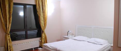 Une chambre avec un lit simple, une table de chevet, une fenêtre avec des rideaux et un radiateur.