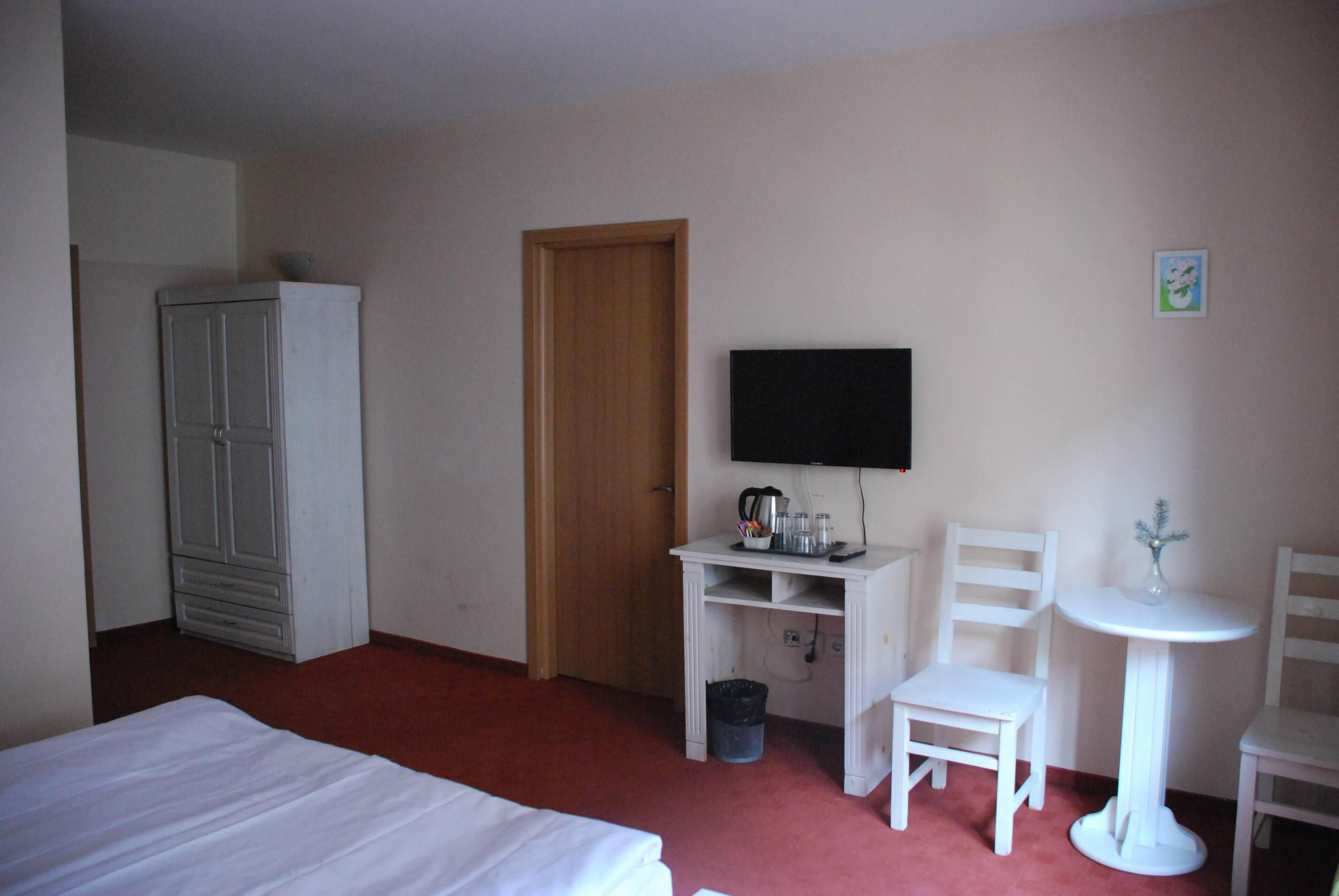 Habitación de hotel con cama, armario, televisor, escritorio con silla y una pequeña mesa con un jarrón.