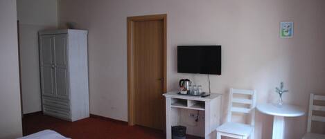 A hotel room with a bed, a wardrobe, a television, a desk with a chair, and a small table with a vase.