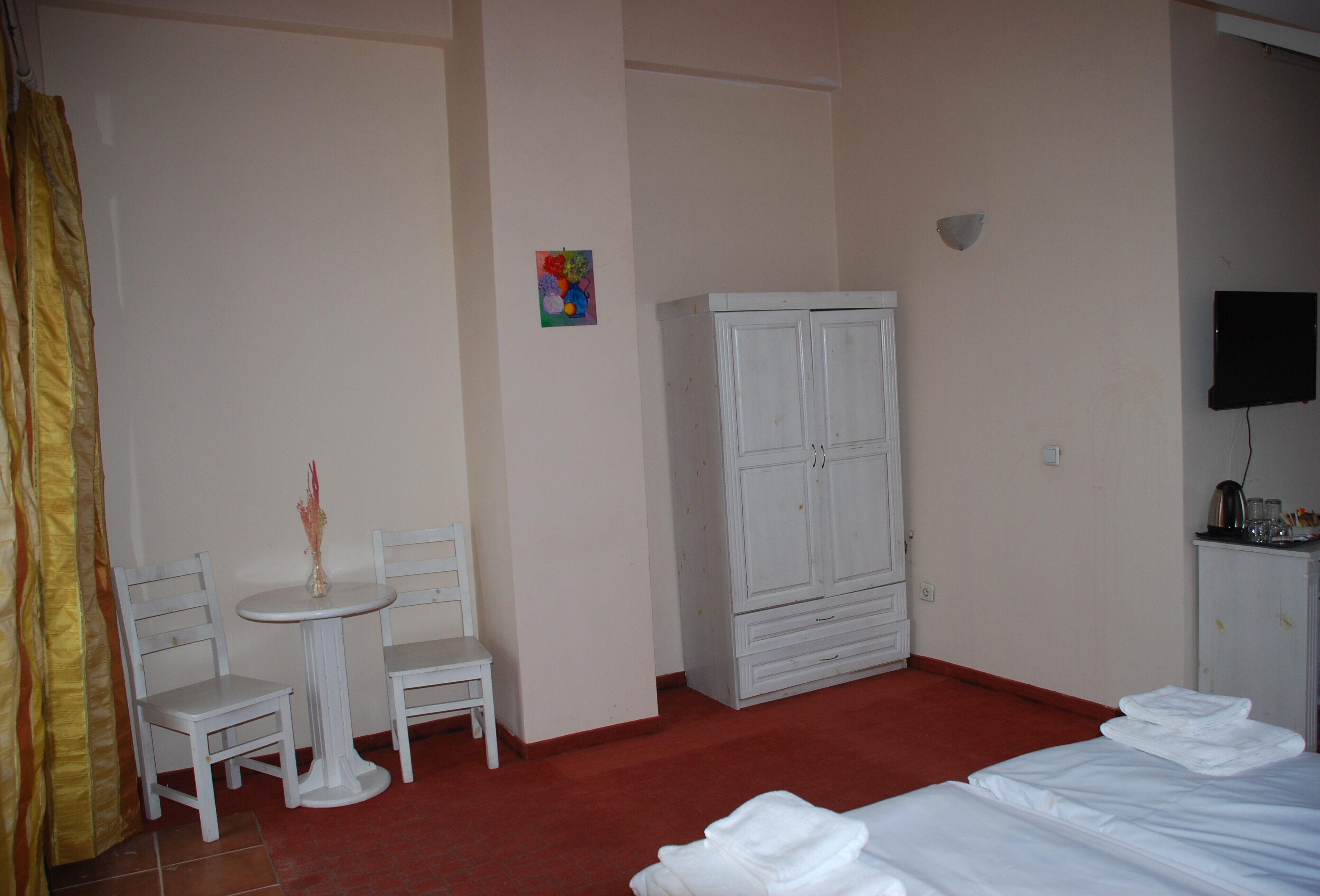 A hotel room with a bed, a small table with chairs, a wardrobe, and a television.