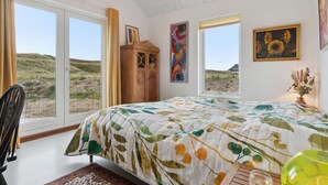 Een slaapkamer met een groot bed, twee ramen, een houten kast en kunstwerken aan de wanden.