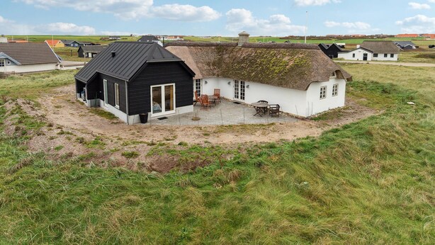 Een rieten huis met een zwart-wit gevel, een omheind terras met buitenmeubels, en een grasveld op de achtergrond.