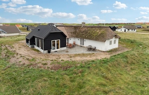 Een rieten huis met een zwart-wit gevel, een omheind terras met buitenmeubels, en een grasveld op de achtergrond.
