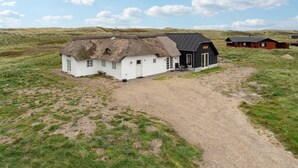 Een huis met rieten dak, een oprit van grind, een zwart gebouw met een bord en een rood gebouw in een grasveld.