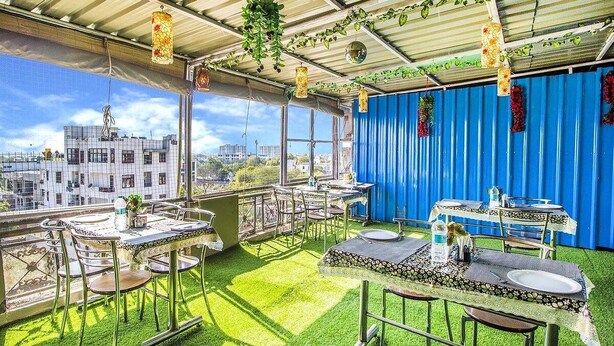 Un espace de restauration en plein air avec des tables et des chaises, une vue sur des bâtiments et un rideau bleu en arrière-plan.