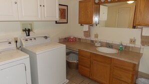 A compact kitchen with a washing machine, wooden cabinets, a sink, and a trash bin.