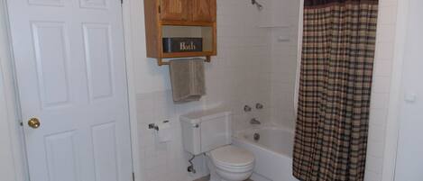 Un baño con inodoro, bañera y un mueble de madera sobre el inodoro.