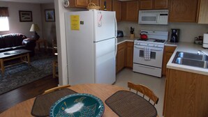 A compact kitchen with wooden cabinets, a white refrigerator, a microwave, and a stove. There is a dining table with two placemats and a chair.