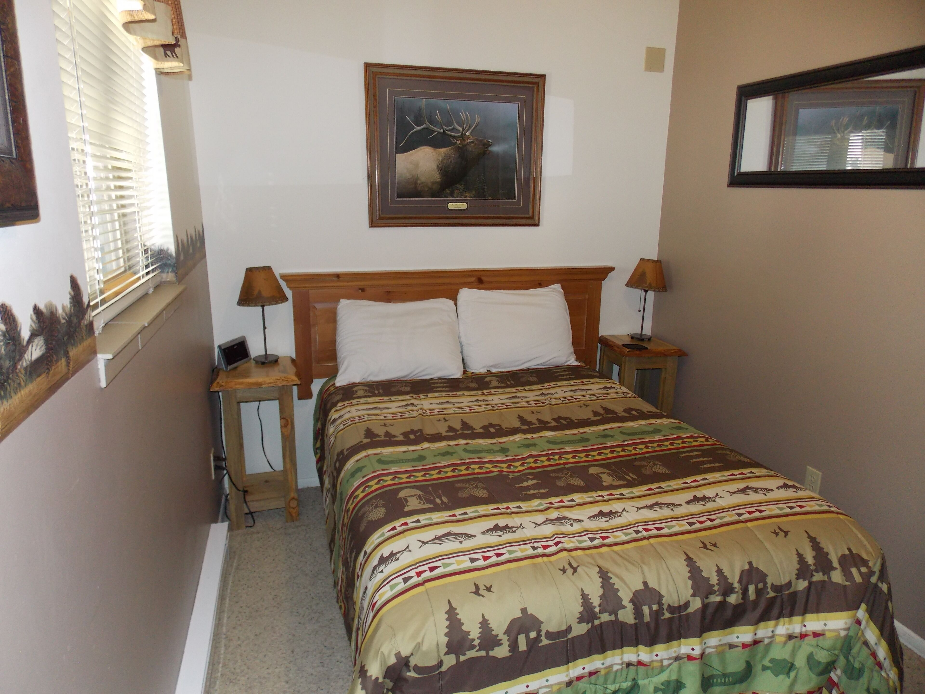 Une chambre à coucher avec un lit, deux lampes de chevet, un tableau représentant un cerf encadré au mur et une fenêtre avec des stores.